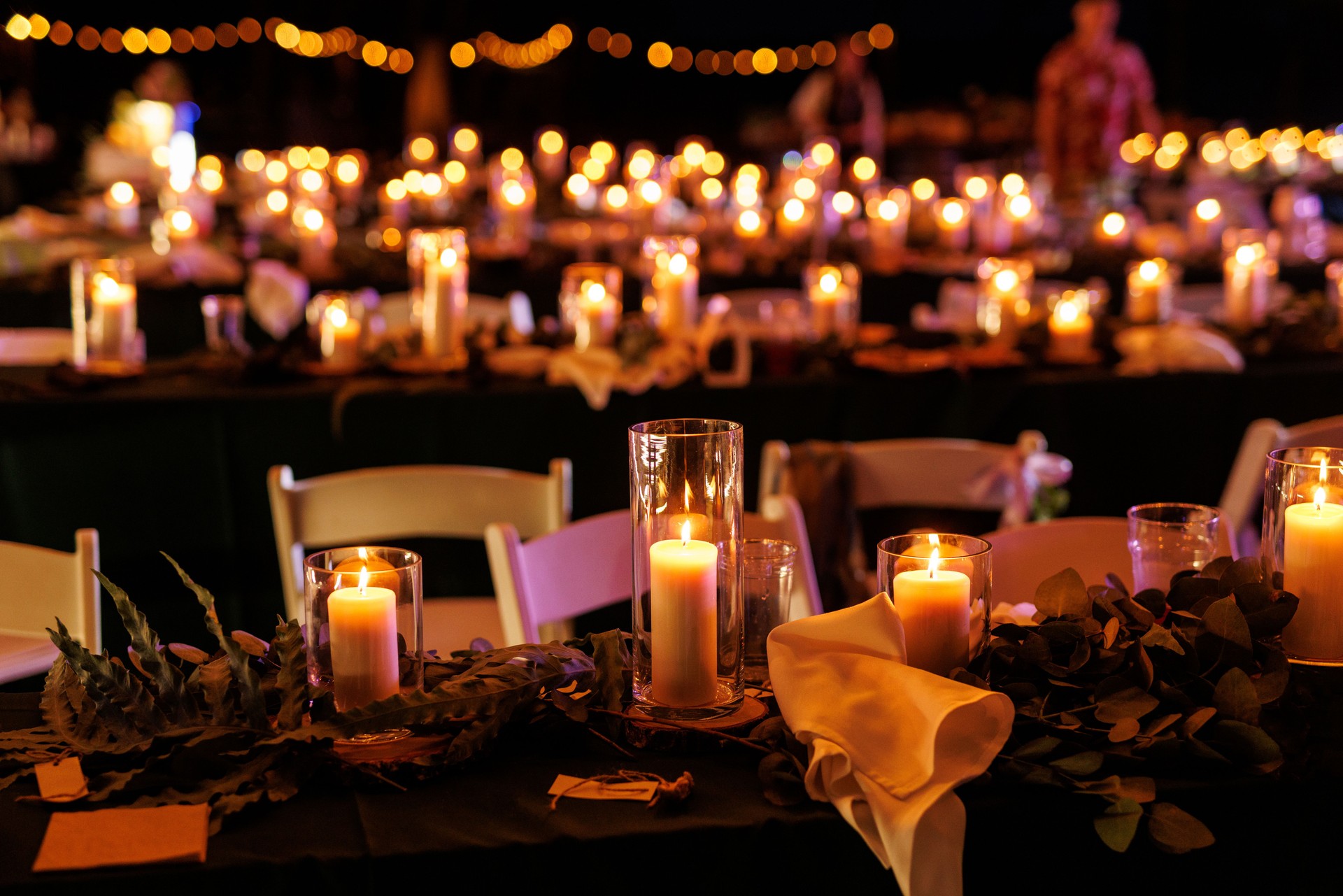 A romantic table setting with lit candles and greenery at a nighttime event.