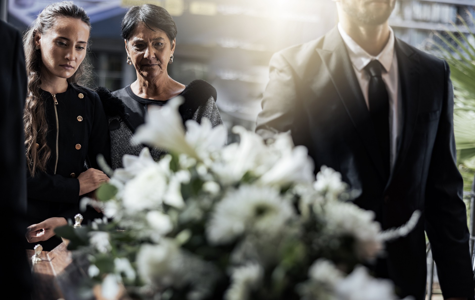 Funeral, coffin and family or friends at death, mourning and church burial event sad together. Depression, grief and christian religion gathering of people and women with support with flowers