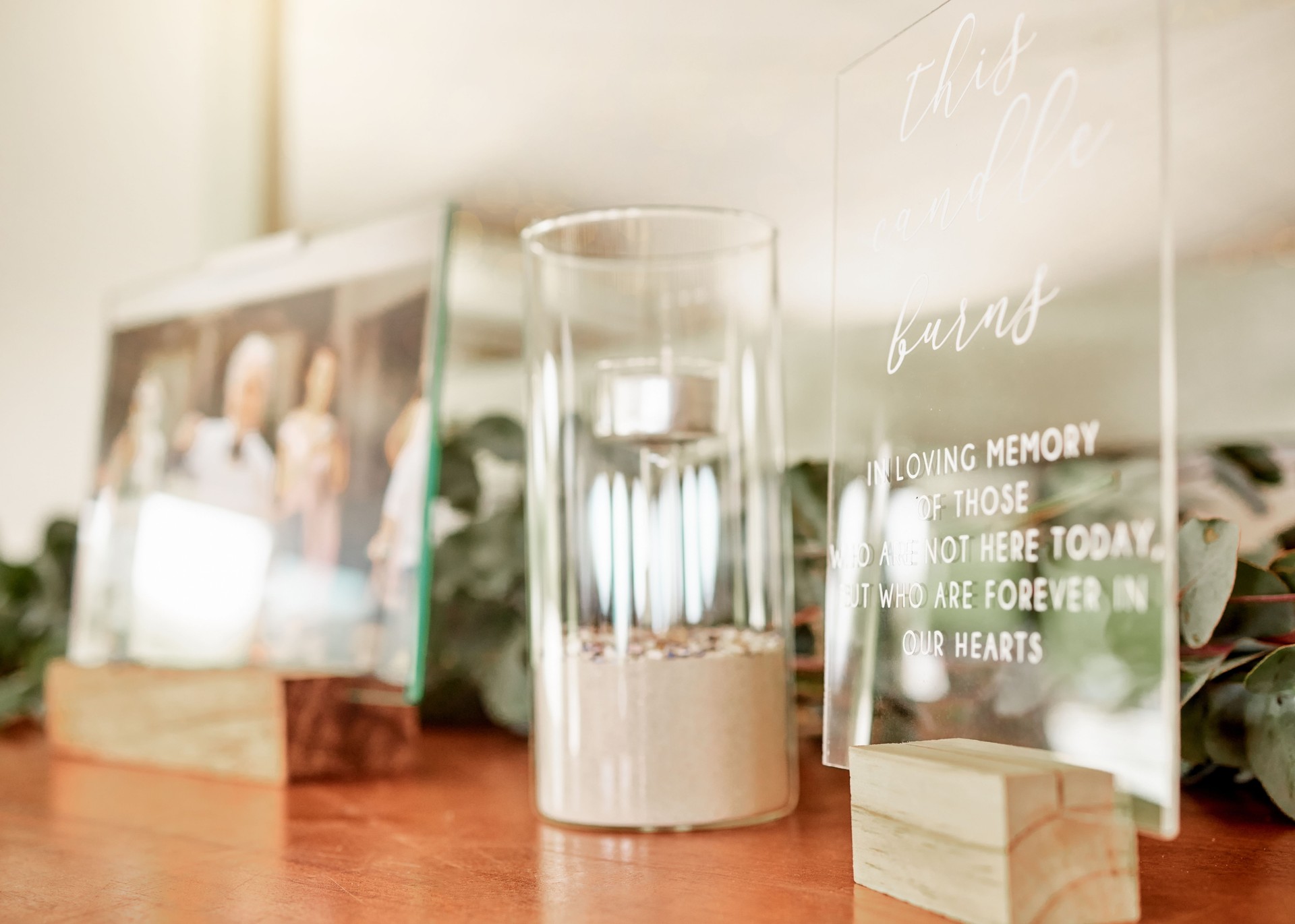 Candle, sad and glass after funeral for memorial, for family or friends in home after death. Grief, loss and picture to show love, care and memory of dead people, on wood mantle in house or apartment